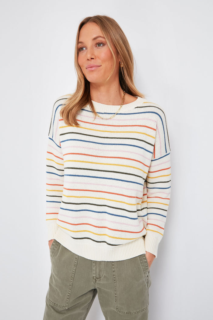 A woman wears an Emerson Fry rainbow-striped sweater and olive green pants, hands in her pockets.