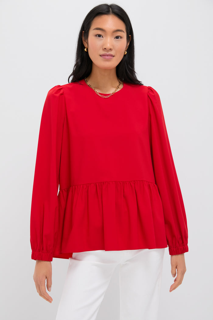 A woman wears a bright red Pomander Place long-sleeve peplum blouse with puff sleeves and a gathered waist, paired with white pants.