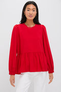 A woman wears a bright red Pomander Place long-sleeve peplum blouse with puff sleeves and a gathered waist, paired with white pants.
