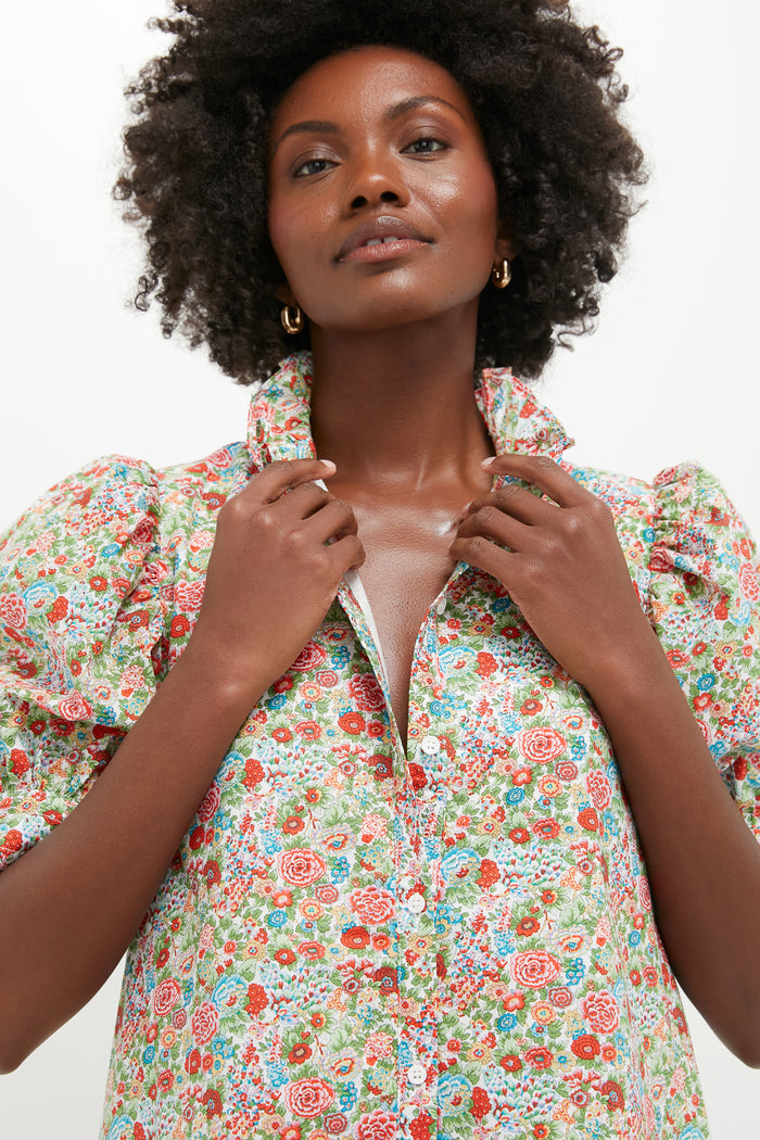 A woman with curly hair wears a Hyacinth House Louisa dress with puffed sleeves, holding the collar and gazing upward.