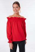 A woman models a Tuckernuck spicy red off-the-shoulder top with ruffle neckline and long sleeves, styled with black pants.