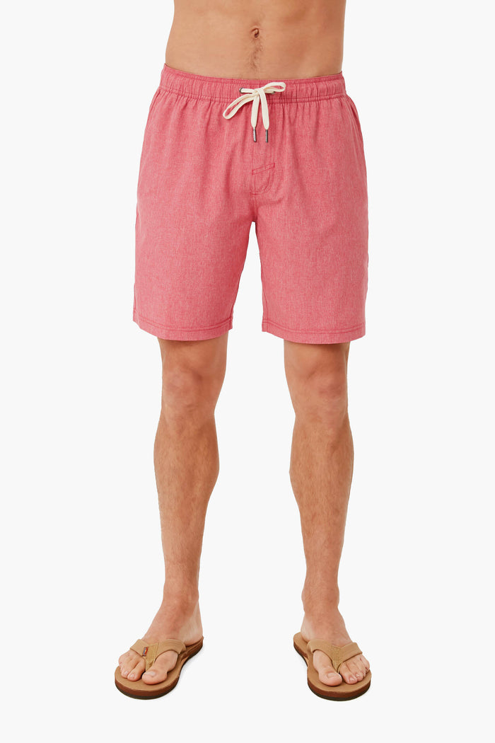 A person in pink Fair Harbor quick-drying recycled swim shorts and brown flip-flops stands confidently, showcasing the stylish look.