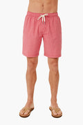 A person in pink Fair Harbor quick-drying recycled swim shorts and brown flip-flops stands confidently, showcasing the stylish look.