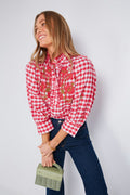 Woman wears an Antik Batik red and white gingham blouse with floral embroidery, blue jeans, and carries a small green handbag.