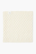 A cream-colored, knitted cormo wool neck gaiter from baa with a ribbed edge and a small white tag featuring a line drawing of a sheep.