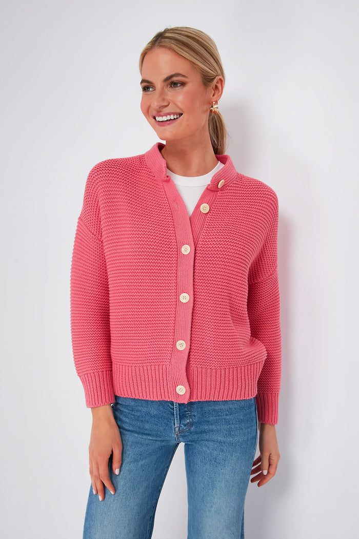 A woman smiles and looks to the side, wearing a pink Alex Mill cotton cardigan over a white top and blue jeans.