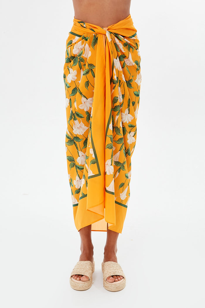 A person wears a yellow floral handmade pareo tied at the waist with beige woven platform sandals, featuring a stylish tropical print coverup from AGUA BY AGUA BENDITA.