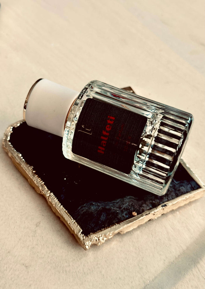 Saffron & Rose Eau de Parfum by LU Fragrances - 50ml bottle lying on its side on a black agate tray, showing ribbed glass and dark label