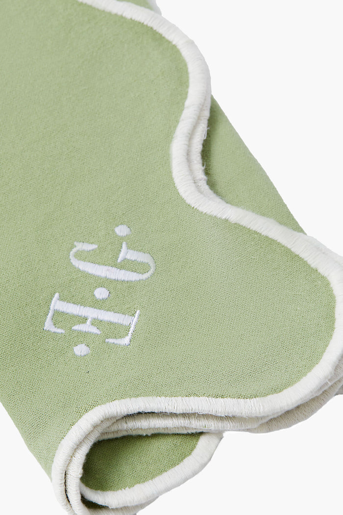 A folded, light green 100% cotton Tuckernuck Home fabric with white trim, contrast thread, and embroidered white J.G. letters on the surface.