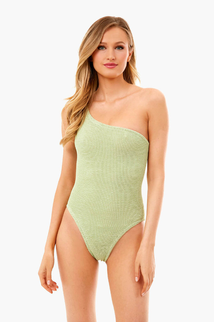 A woman wears a Hunza G light green one-shoulder swimsuit featuring a crinkle-stretch texture and high-cut legs.