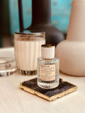 Sandalwood & Cardamom Eau de Parfum by LU Fragrances — 50ml glass bottle lying on its side on a gold-edged black stone coaster, with a white candle and ceramic vases in soft focus behind