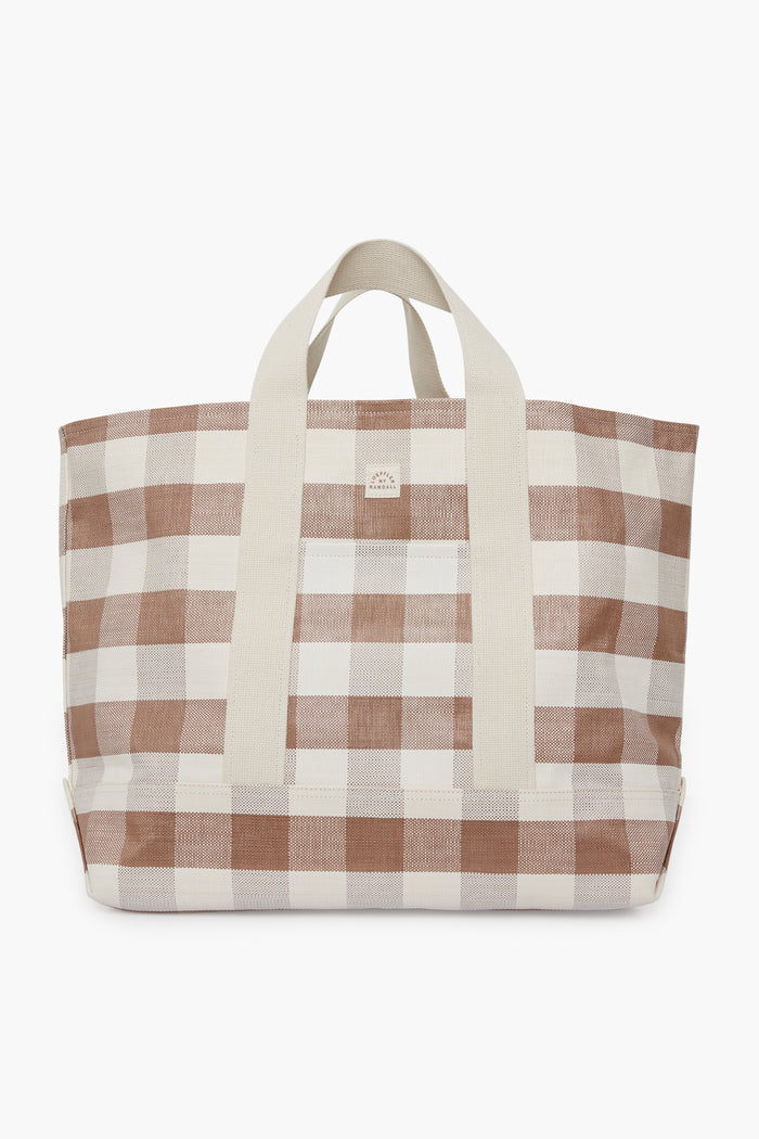 The Loeffler Randall oversized tote features a beige and white checkered pattern, cream cotton woven handles, and a central logo patch, combining style with functionality.