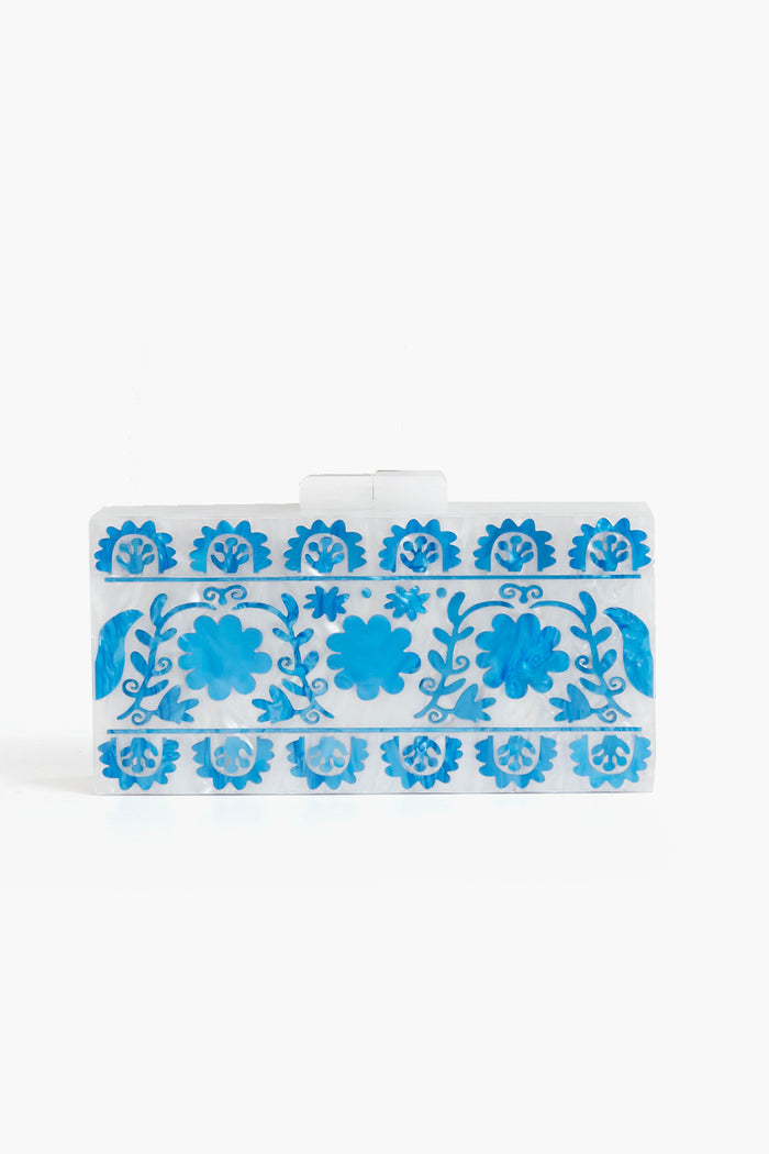 The ASHA Sardinia Clutch is a chic rectangular box clutch in white, adorned with blue floral and leaf patterns and finished with a clear clasp.
