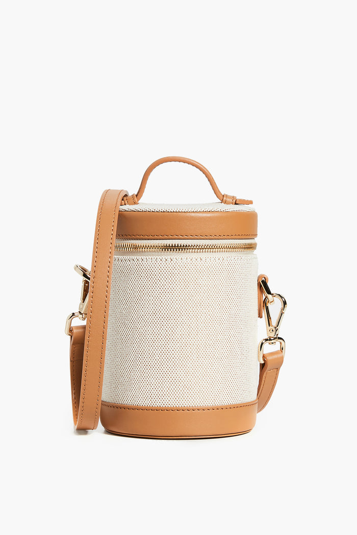 The Paravel bag is lightweight with a structured cylindrical shape, tan leather handle and trim, white textured body, and a detachable tan strap accented by gold-tone hardware.