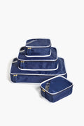 Four Paravel navy blue packing cubes with white trim and gold zippers are stacked on a white surface; one multifunctional storage cube is in front, partially unzipped to show its contents.