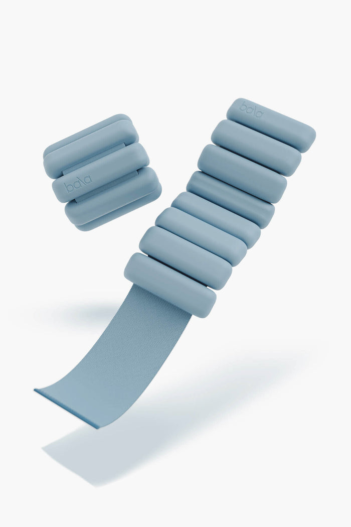 A pair of bala light blue adjustable wrist or ankle weights with segmented cylindrical padding and Velcro strap—perfect wearable fitness accessories.