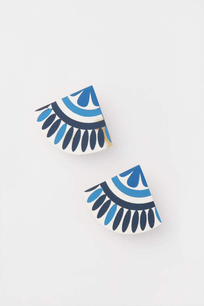 Sunshine Tienda offers lightweight earrings crafted from buffalo horn, featuring two semi-circular shapes adorned with blue, black, and white geometric patterns for a unique look.