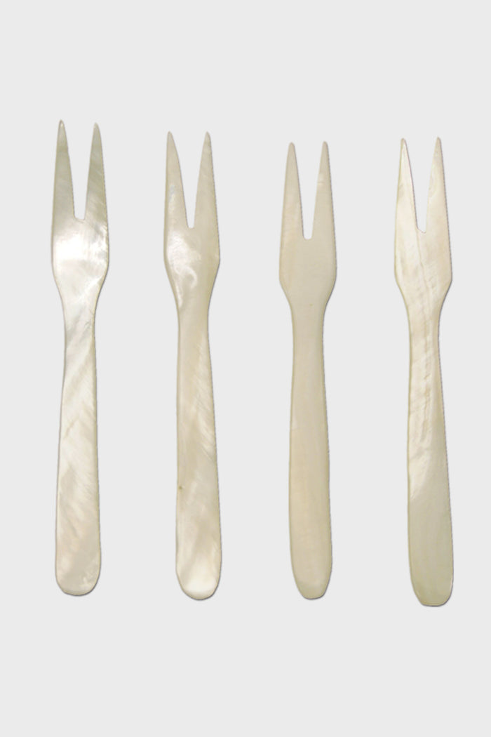 Four small, two-pronged, white mother-of-pearl seashell forks by Be Home are arranged in a row—perfect for coastal dining and for adding ethically sourced elegance to your home.