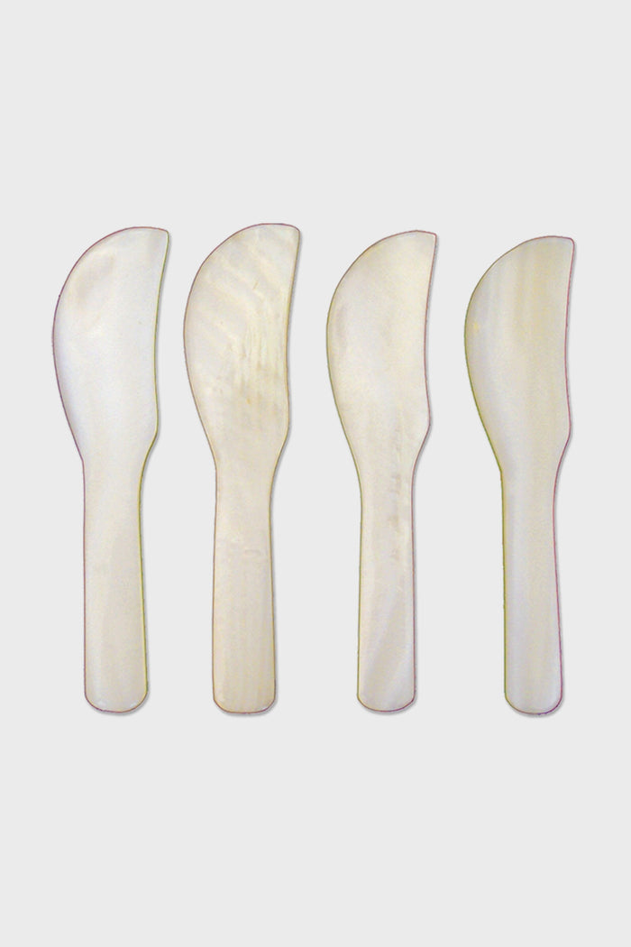 Four pearlescent, flat, curved butter knives by Be Home, crafted from Mother of Pearl and arranged vertically side by side—an elegant addition to ethically sourced home goods.