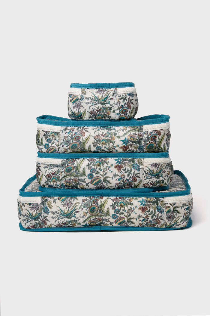 Four rectangular fabric storage boxes from Tuckernuck Accessories feature blue edging and a floral print. Stacked from largest to smallest, they make stylish packing cubes—ideal travel essentials—shown on a plain white background.
