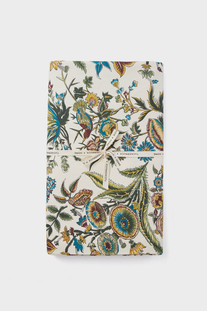 A rectangular gift wrapped in white paper with colorful floral and bird patterns, tied with a text-printed white ribbon—perfect inspiration for a Tuckernuck Home cotton rectangle tablecloth design.
