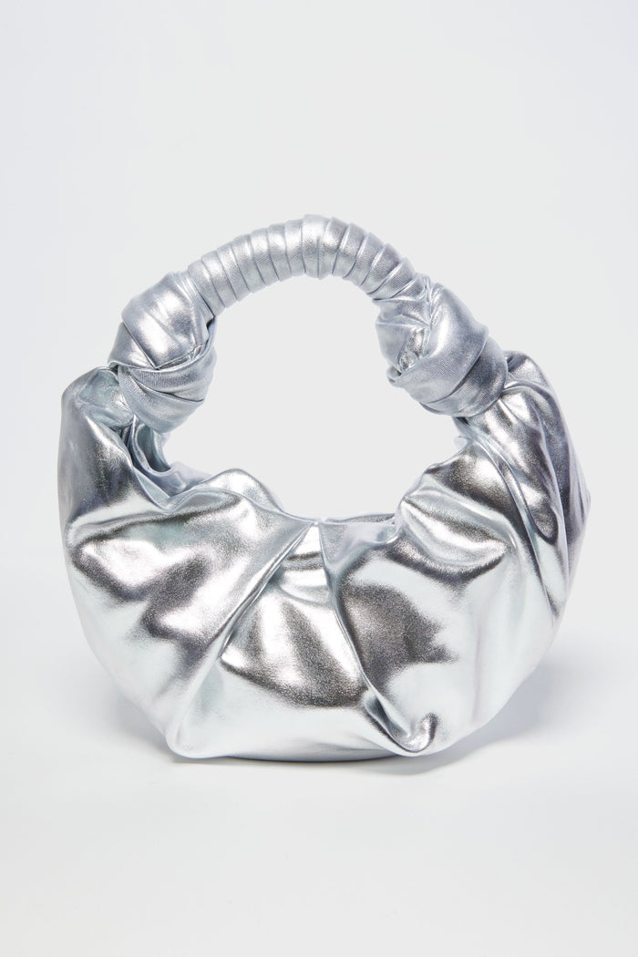 The Simon Miller Lopsy Bag is a small, silver statement purse crafted from metallic vegan leather with a scrunched, knotted handle and a shiny, crinkled texture.