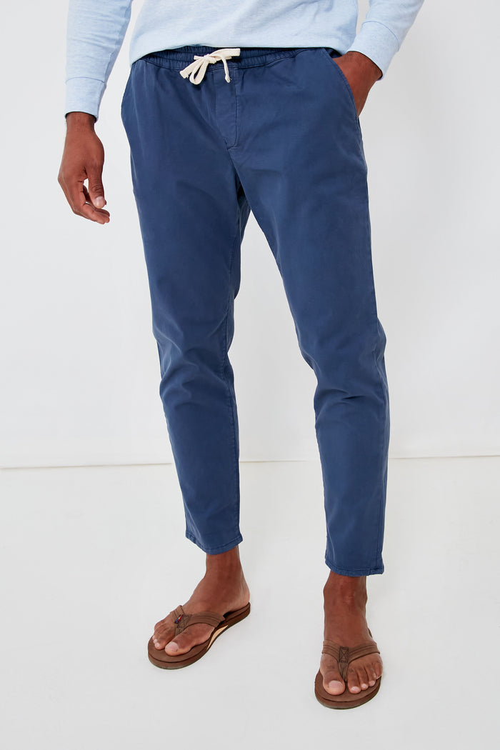 A person confidently showcases a comfortable and modern look in Marine Layer blue athletic fit pants, a light blue long-sleeve shirt, and brown flip-flops.