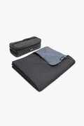 A folded dark gray YETI Lowlands Blanket with a light gray interior and a YETI label sits beside its matching zippered case. This insulated picnic blanket by YETI offers outdoor comfort and durability.