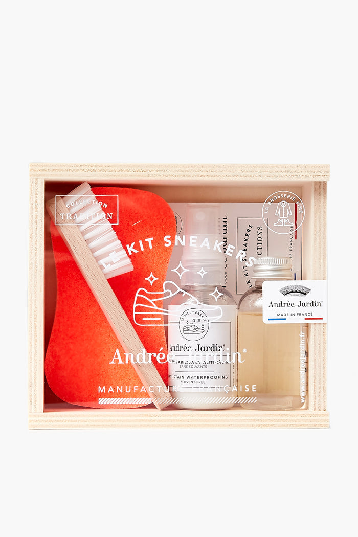 An Andree Jardin wooden box contains a sneaker care kit with a brush, orange sponge, shoe cleaning solution, waterproofing spray, and cloth.