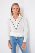 A woman models the Varley Snow White Calva Knit, a textured open-knit zip-up sweater with a navy V pattern, paired with light blue jeans—highlighting women’s performance fashion.