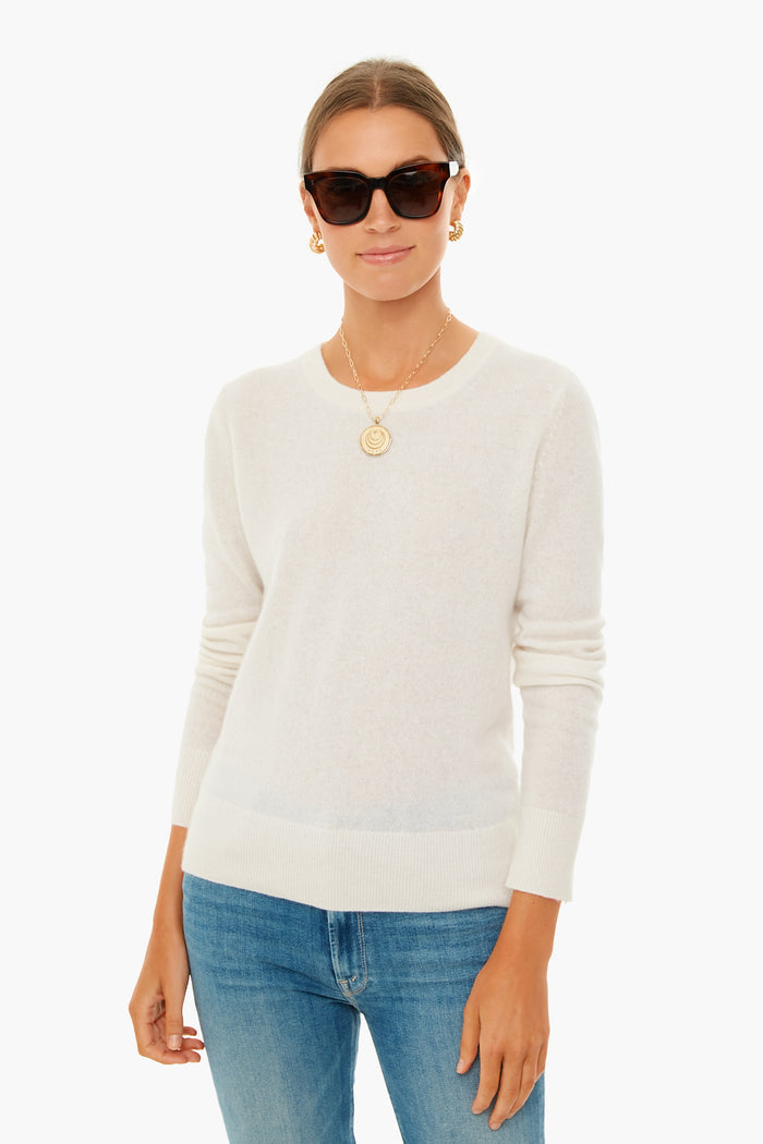 Wearing a White + Warren cashmere long-sleeve sweater, blue jeans, gold earrings, a pendant necklace, and dark sunglasses, this person confidently showcases modern closet staples.