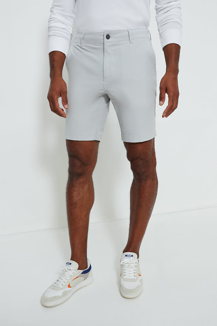 A man wears a Faherty white long-sleeve shirt, light gray quick-dry recycled polyester shorts, and white sneakers with orange and navy accents.
