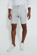 A man wears a Faherty white long-sleeve shirt, light gray quick-dry recycled polyester shorts, and white sneakers with orange and navy accents.