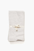 A neatly folded light gray Stone Washed Linen Napkin from Farmhouse Pottery, Inc is tied with a cream-colored ribbon labeled Farmhouse Pottery.