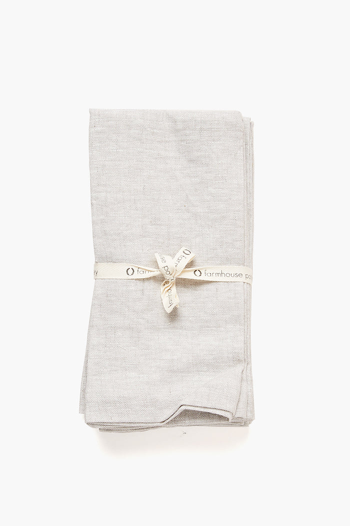 A neatly folded light gray Stone Washed Linen Napkin from Farmhouse Pottery, Inc is tied with a cream-colored ribbon labeled Farmhouse Pottery.
