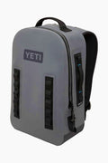 A gray YETI Panga Backpack with black straps, a top handle, and a front zipper pocket stands upright—an ultra-durable, waterproof backpack ideal for outdoor adventures.