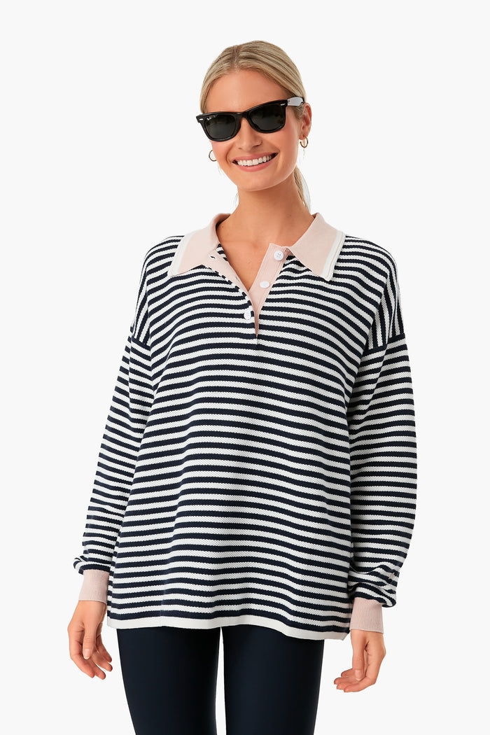 A woman smiles confidently in The Upside’s Norfolk Wonder Polo—black-and-white stripes with light pink collar and cuffs—and black sunglasses. This organic cotton polo blends style with comfort.