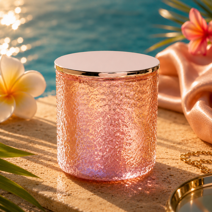 Rose gold candle with a textured surface on a sandy background with flowers and jewelry.