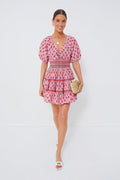 A woman wears a Saylor pink boho-chic mini dress with puffy sleeves, paired with white sandals and a small woven clutch.