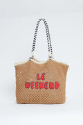 A Clare V woven straw summer bag features black and white striped handles and red "LE WEEKEND" lettering on the front, inspired by the iconic Clare V tote.