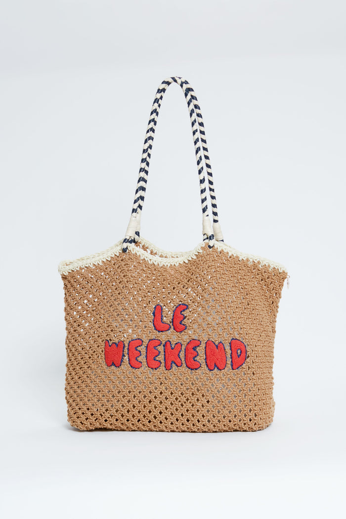 A Clare V woven straw summer bag features black and white striped handles and red "LE WEEKEND" lettering on the front, inspired by the iconic Clare V tote.