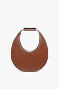 STAUD's Tan Moon Tote is a brown, crescent-shaped leather shoulder bag with a short, wide top handle.