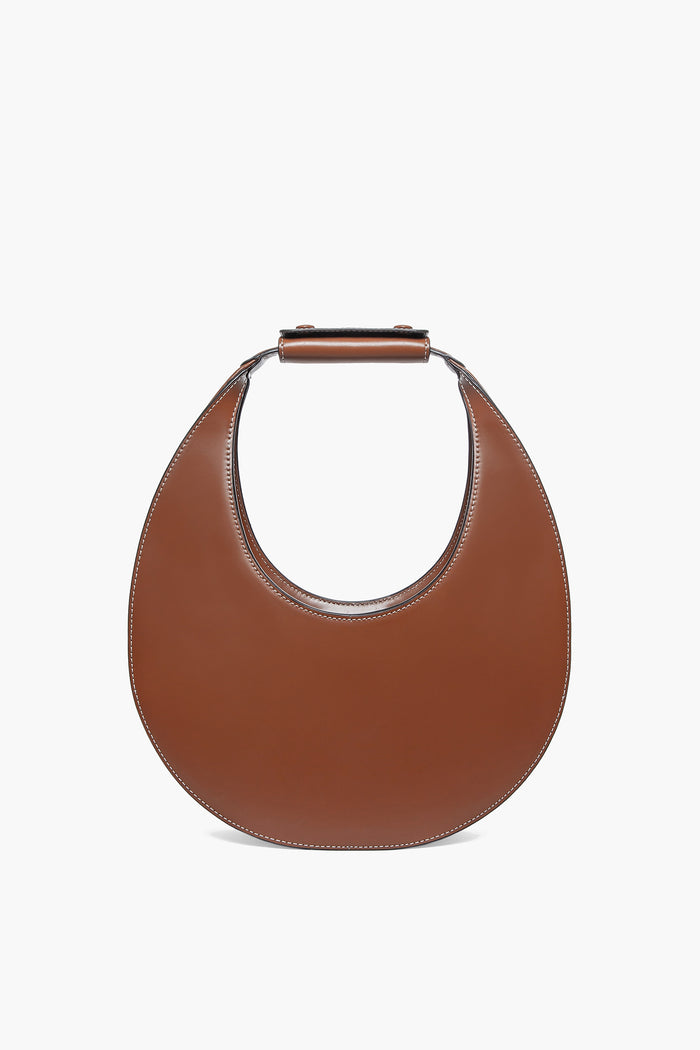 STAUD's Tan Moon Tote is a brown, crescent-shaped leather shoulder bag with a short, wide top handle.