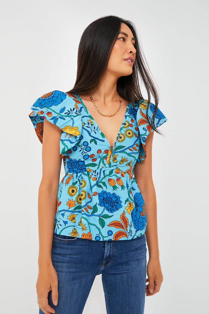 A woman wears a vibrant floral top by Love the Label, featuring ruffle sleeves, a V-neck, and a fitted waist, paired with blue jeans.