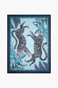 Vibrant illustration of two leopards with patterned fur, set amid blue and green tropical leaves and a decorative frame—inspired by South African artistry and the Ardmore Design Tanzanite Cheetah Kings Tea Towel.