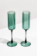 Two FAZEEK champagne flutes with green-tinted, scalloped edges and a subtle wave design are arranged on a white surface.