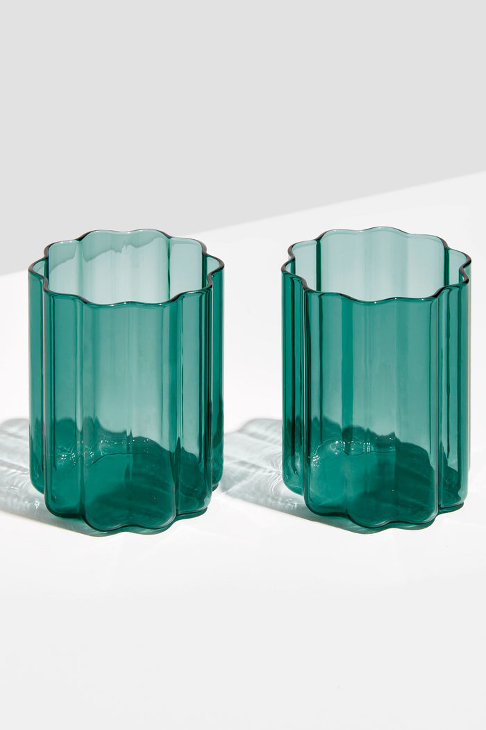 Two green, translucent scalloped tumblers by FAZEEK, crafted from hand-blown borosilicate glass, sit side by side on a white surface.