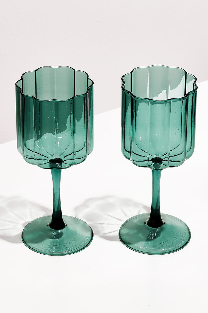 Two FAZEEK Teal Wave Wine Glasses with green-tinted, scalloped edges and textured sides, crafted from hand-blown borosilicate glass, rest on a white surface.