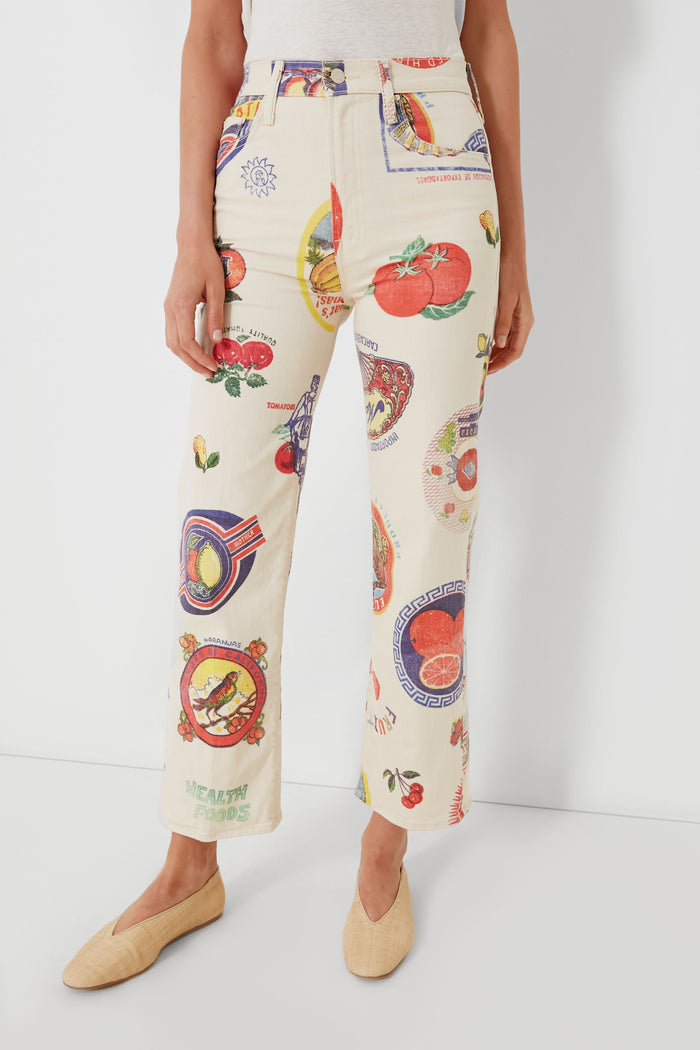 A person wearing MOTHER cream-colored high-waisted jeans featuring a vibrant fruit sticker print, visible from waist to ankles.