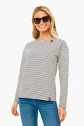 A woman wearing KULE sunglasses and a 100% cotton black and white striped tee with embroidered patches, paired with blue jeans, stands smiling.
